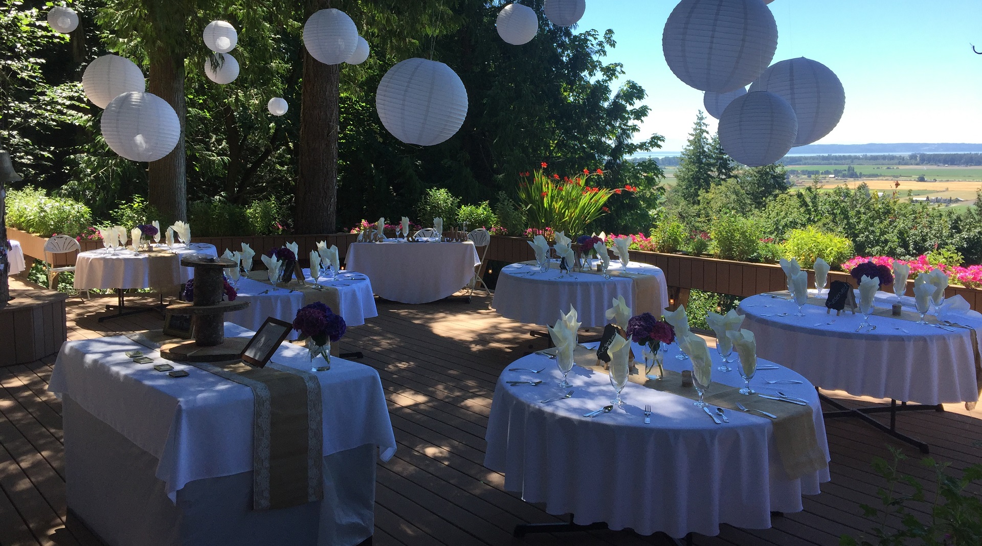 A group of tables with white linen and paper lanterns hanging from the ceiling.