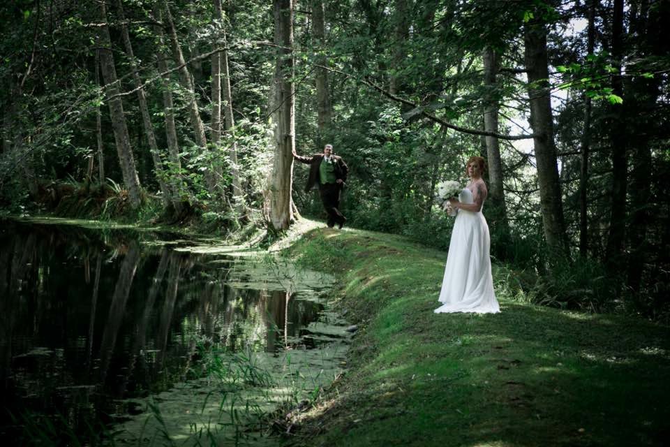 A bride and groom in the woods near water.