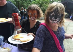 Two women with face paint eating a sandwich.
